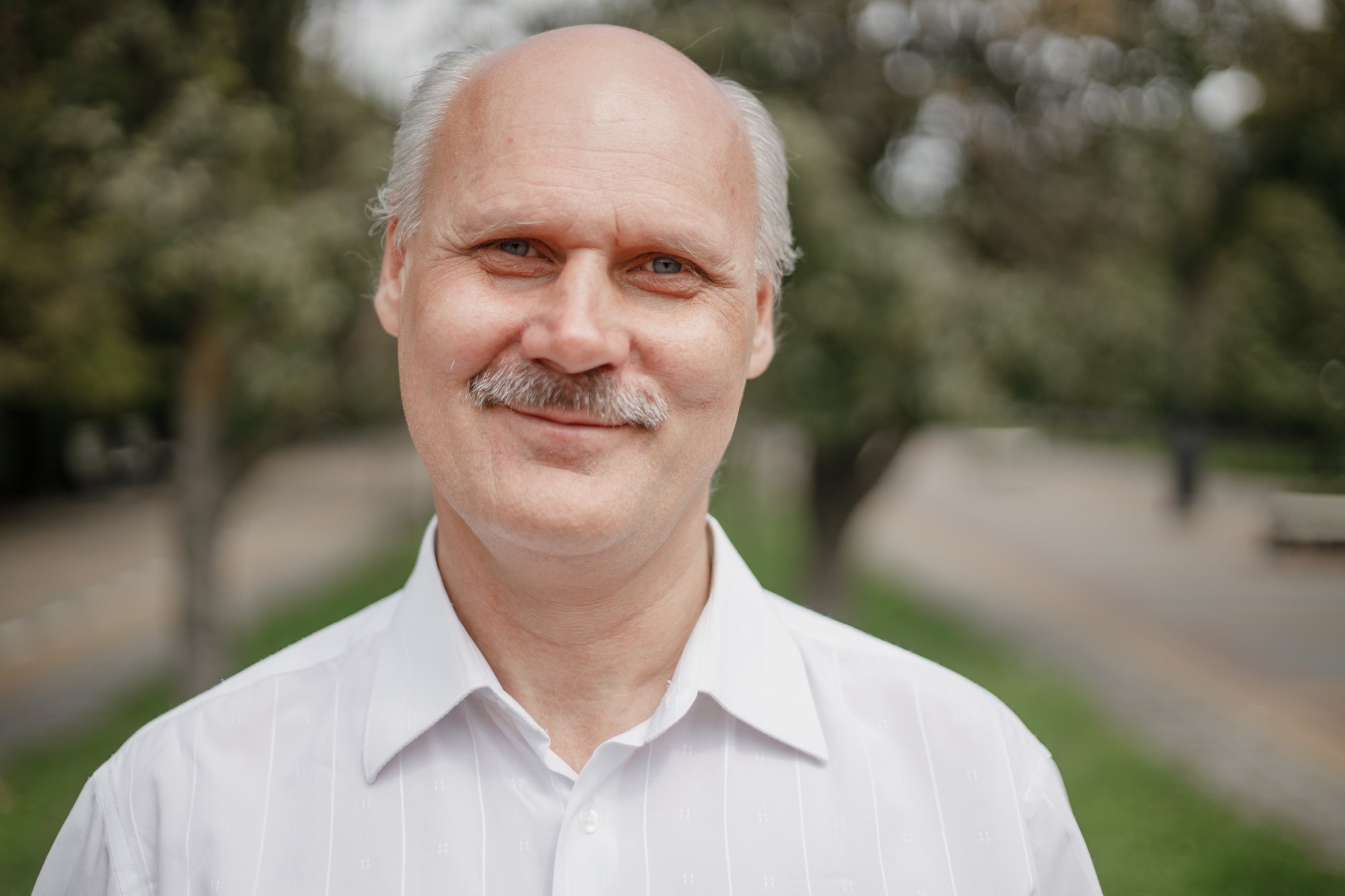 Photo portrait of a smiling old man in the white shirt in a park on a warm day